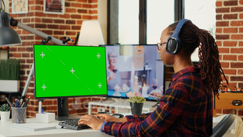 Female freelancer wearing headphones and using greenscreen stock photo NULLED