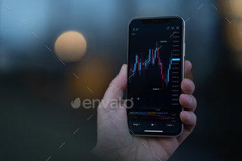 Trader looking at mobile phone with stock chart on screen stock photo NULLED